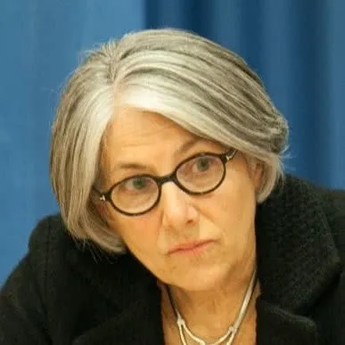 Portrait of a woman with short gray hair and glasses, wearing a black jacket, seated indoors