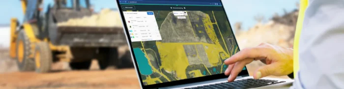 Worker using a laptop outdoors with Picterra platform analyzing mining site maps in front of excavation machinery