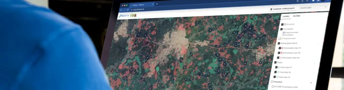 Close-up of a computer screen displaying the Picterra platform with deforestation alerts, forest layers, and supply chain monitoring maps