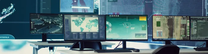 Row of computer monitors displaying maps, satellite imagery, and environmental monitoring dashboards in a control room