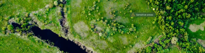Aerial view of a mixed landscape showing grassland, wetlands, and forest edges with a highlighted “sensitive areas” indicator, illustrating biodiversity monitoring using geospatial analysis.